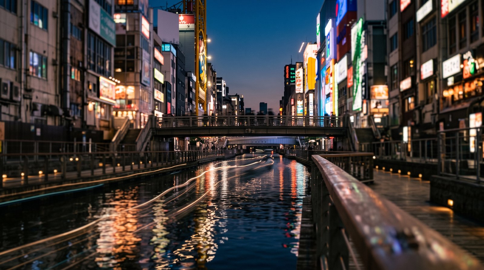 大阪・道頓堀川沿いの夕暮れ。両岸の商業ビルのネオンが水面に反射している風景